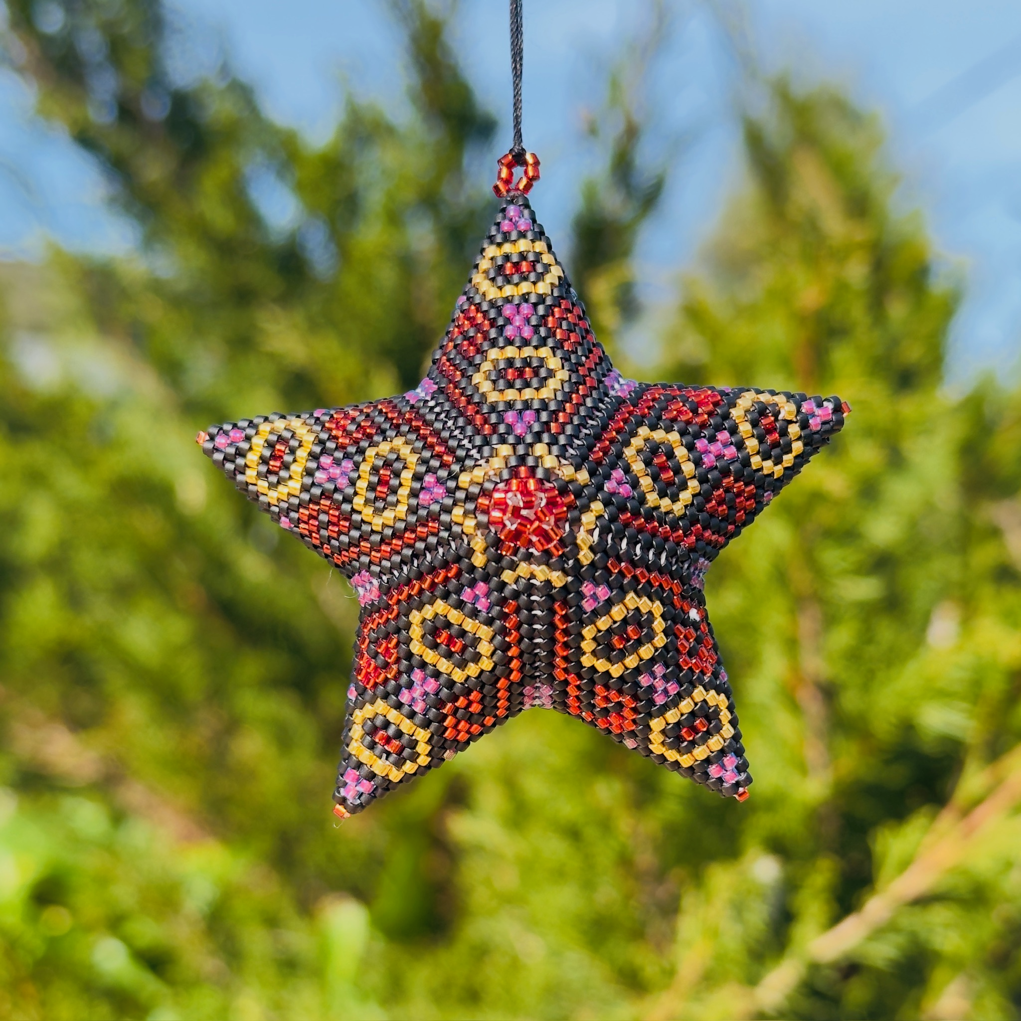 Beaded star ornament with bold red, pink, and gold geometric pattern hanging outdoors